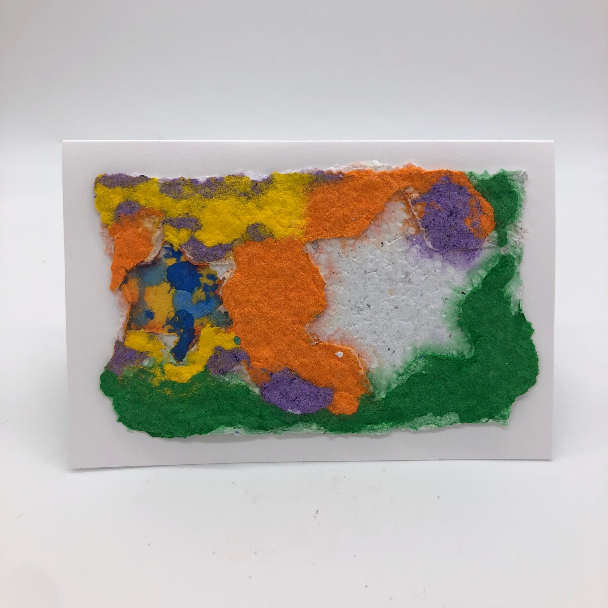 Handmade paper greeting card made with several colors including orange, green, yellow, purple and blue.  On top are two Stars of David.   One is solid white, the other has several colors on the inside.