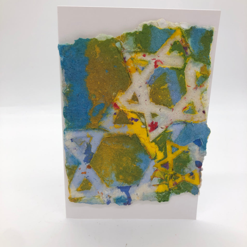 Handmade paper card with three outlined star of David on top.  Paper is green, yellow and blue with a little red mixed in.