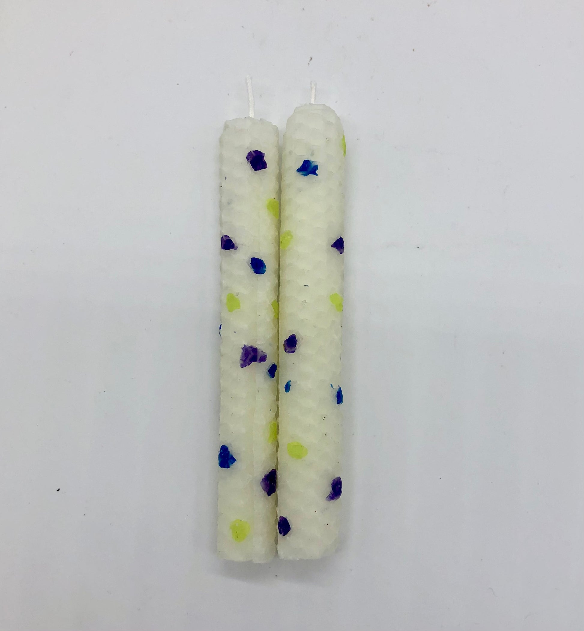 Two white shabbat candles with dots of color in blue, purple and chartreuse.
