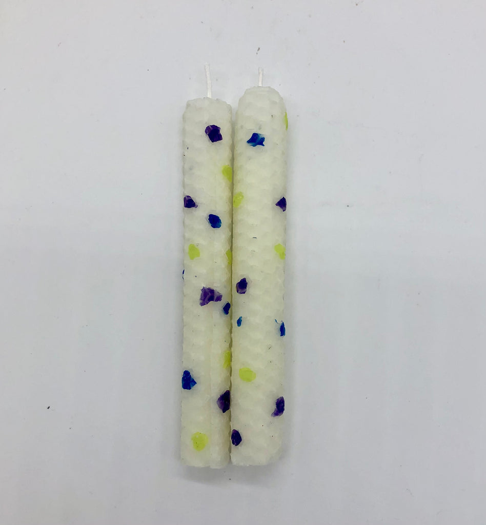 Two white shabbat candles with dots of color in blue, purple and chartreuse.