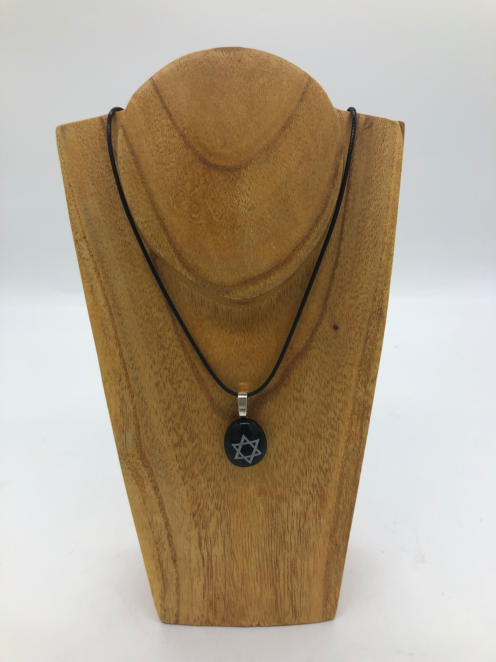 Fused glass necklace on a black cord, displayed on wooden holder.  Necklace design is a black circle with white star of David. center.