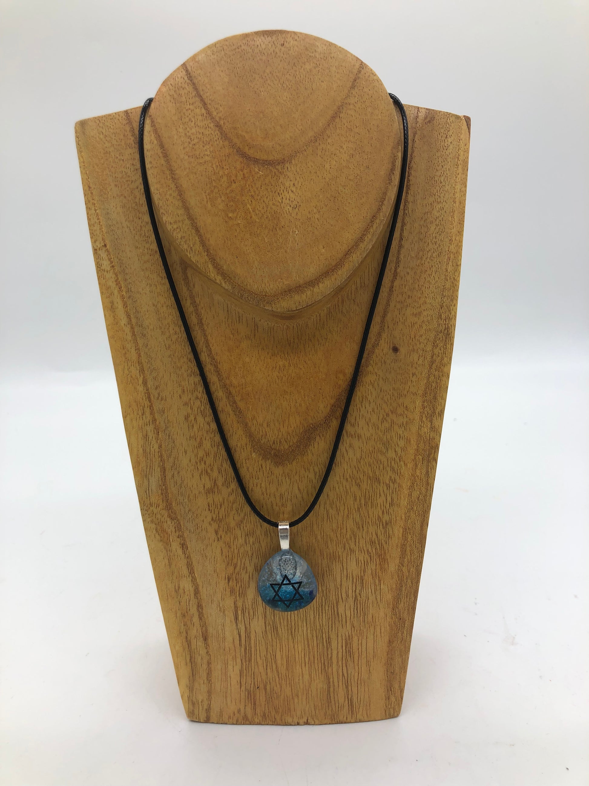 Fused glass necklace on a black cord, displayed on wooden holder.  Necklace design is a clear and blue circle with black star of David. 