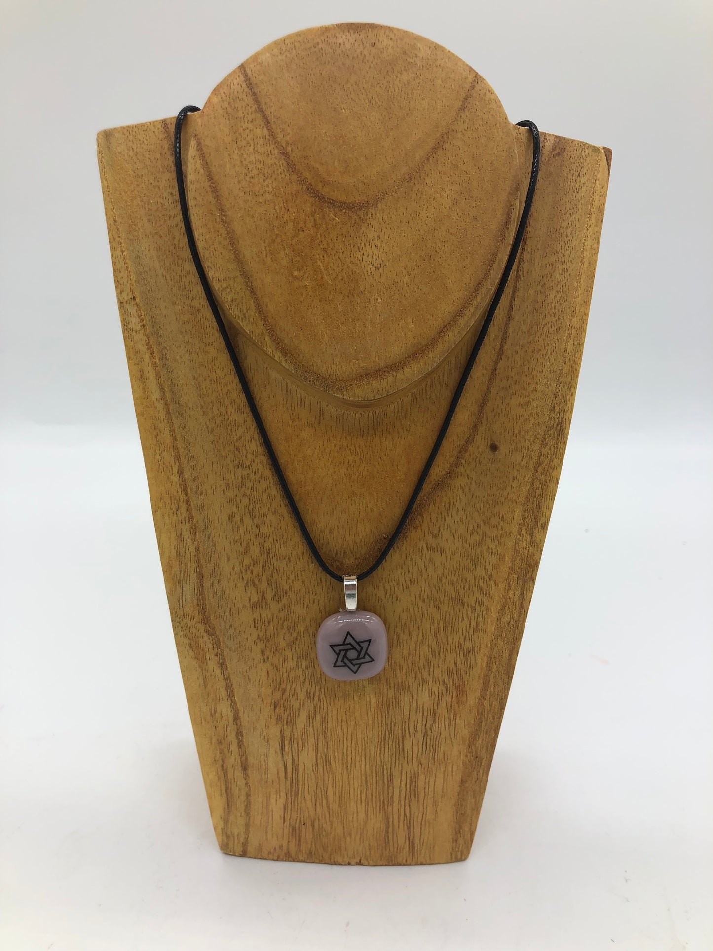 Fused glass necklace on a black cord, displayed on wooden holder.  Necklace design is a mauve  circle with outlined black star of David. 