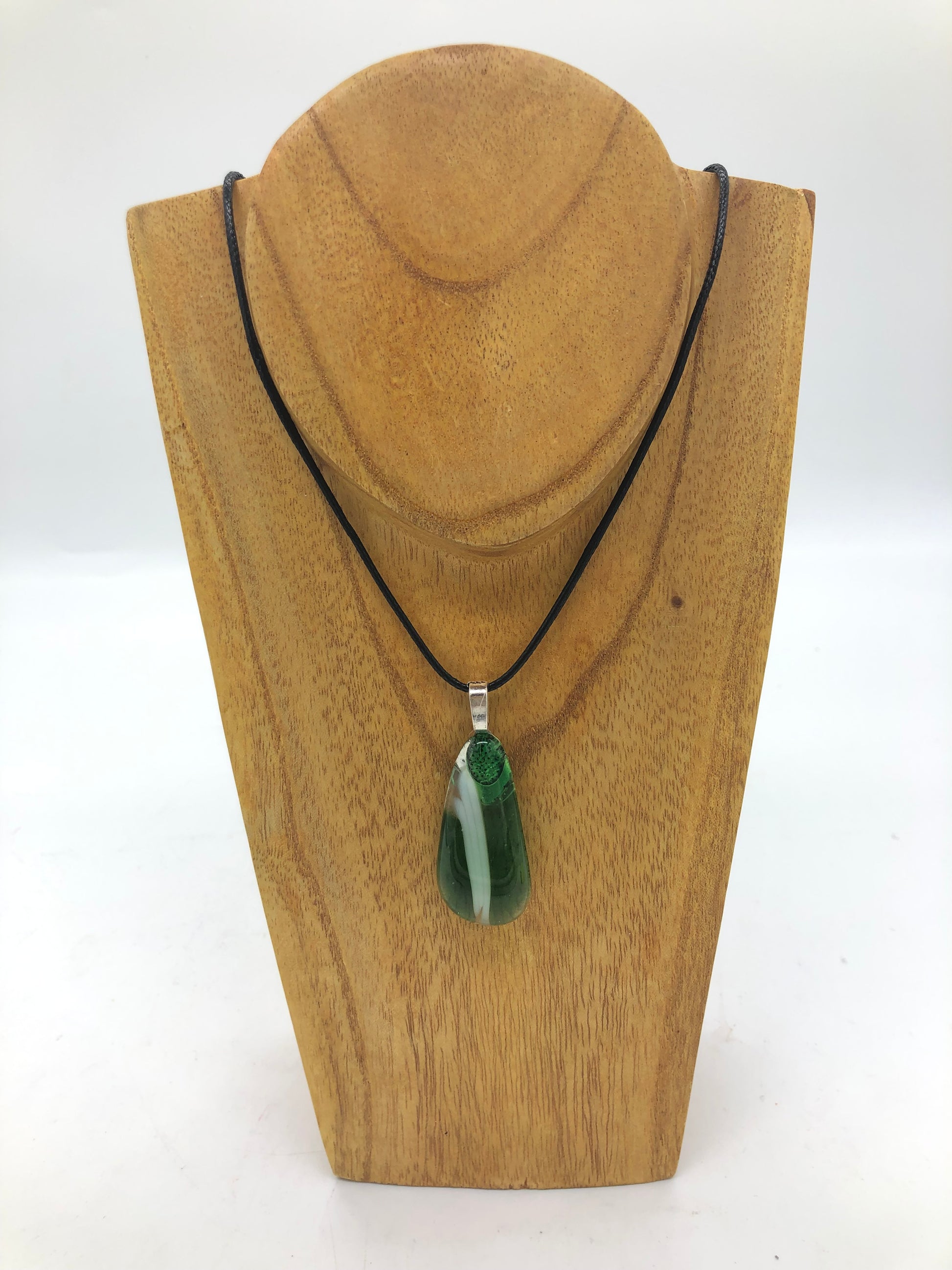 Fused glass necklace on a black cord, displayed on wooden holder.  Necklace design is along oval in green and white