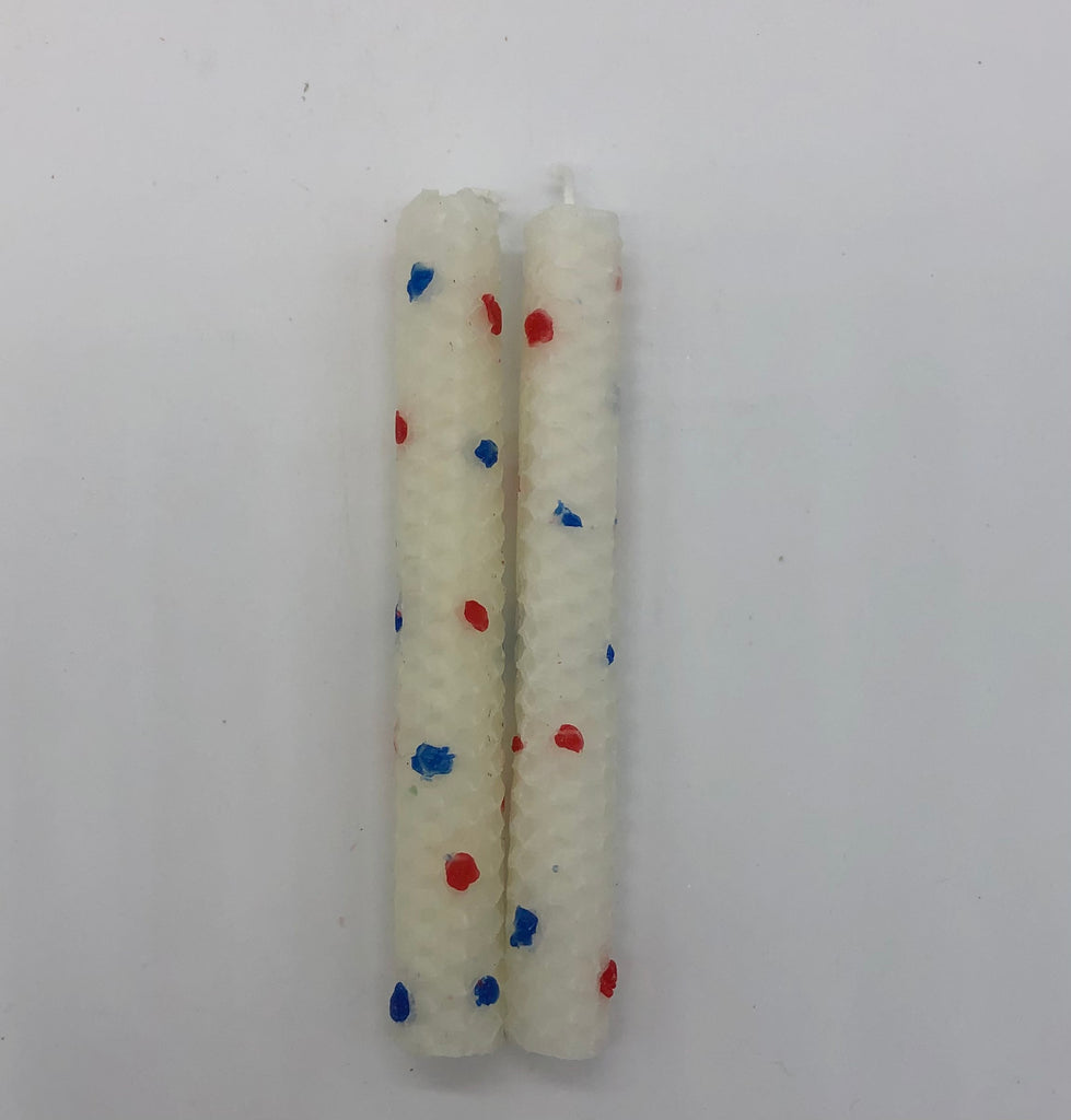 Two white shabbat candles with dots of color in red and blue.