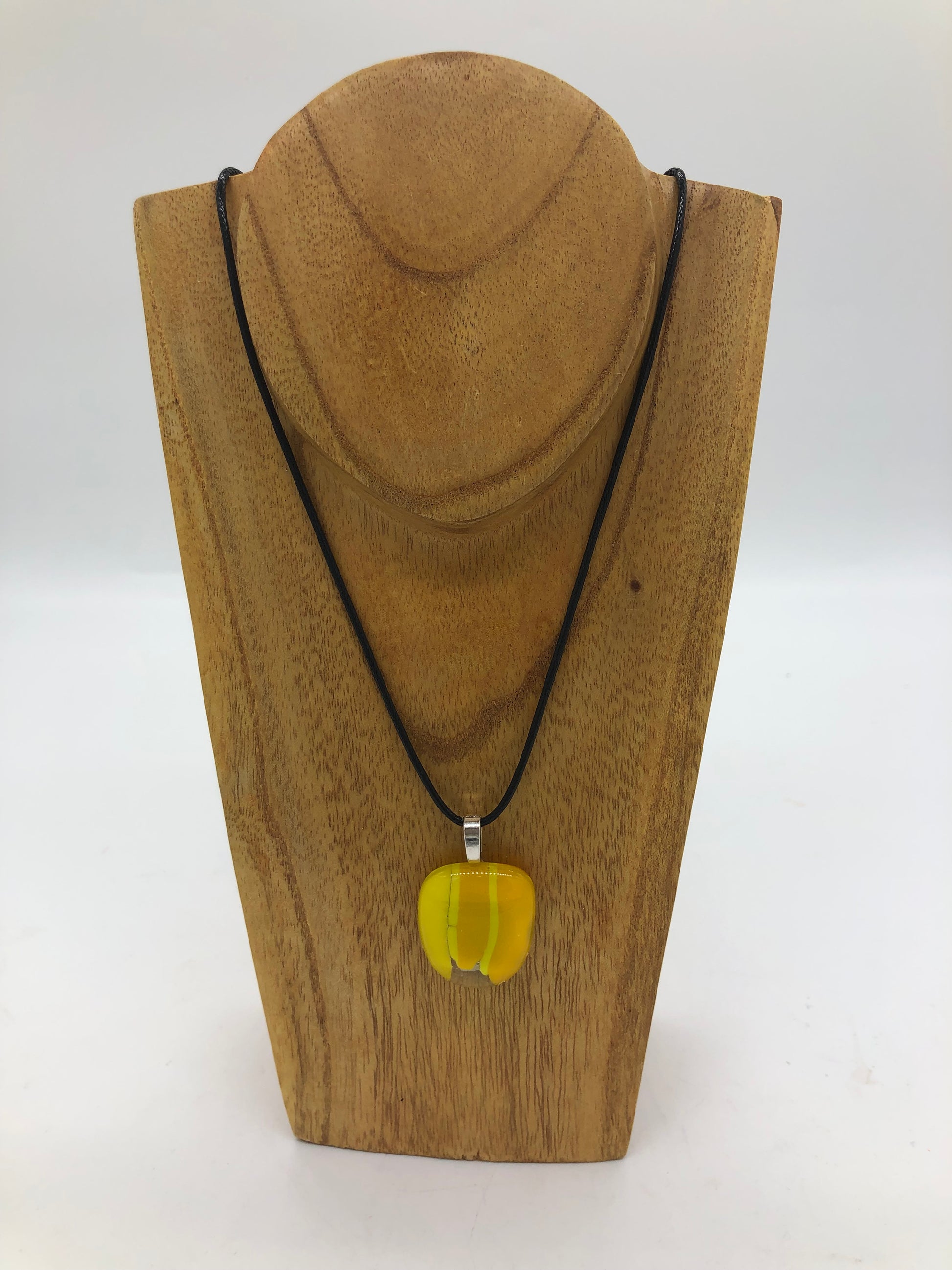 Fused glass necklace on a black cord, displayed on wooden holder.  Necklace design is a clear rounded square with two shades of yellow stripes.. 