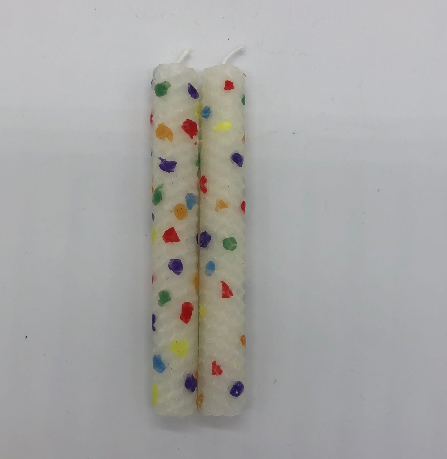Two white shabbat candles with dots of color in rainbow colors.
