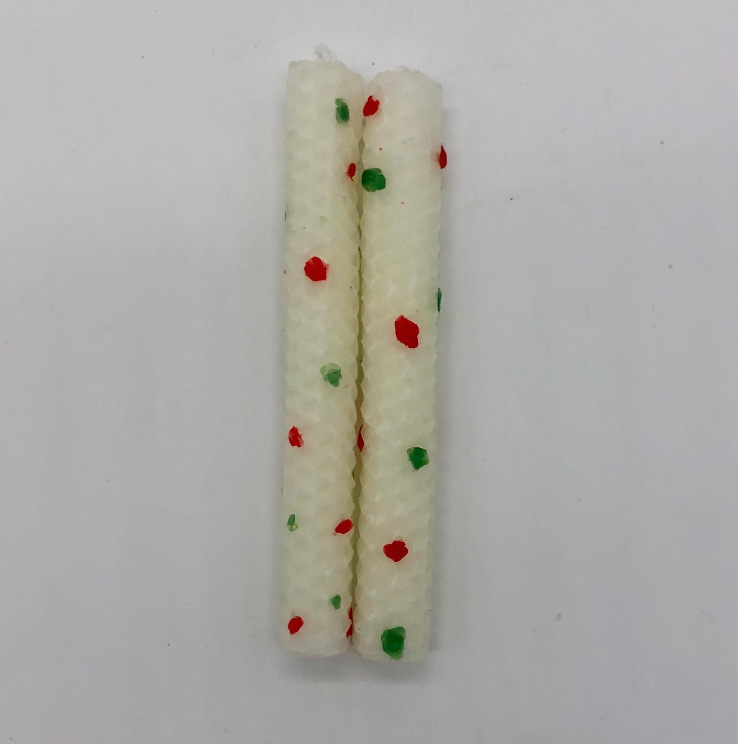 Two white shabbat candles with dots of color in red and green.