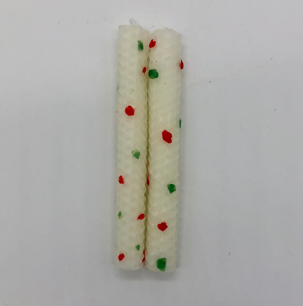 Two white shabbat candles with dots of color in red and green.