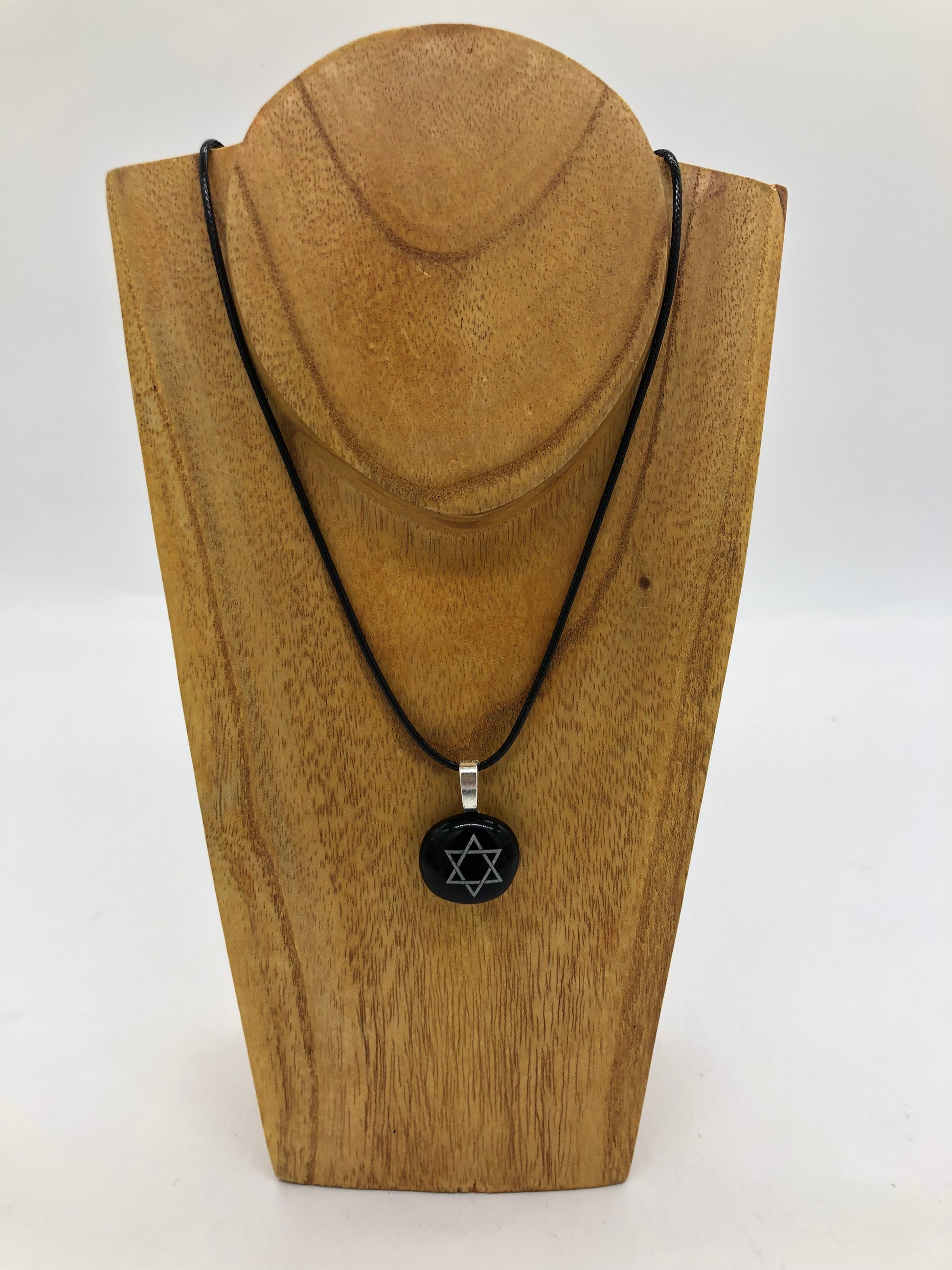 Fused glass necklace on a black cord, displayed on wooden holder.  Necklace design is a black circle with white star of David. 