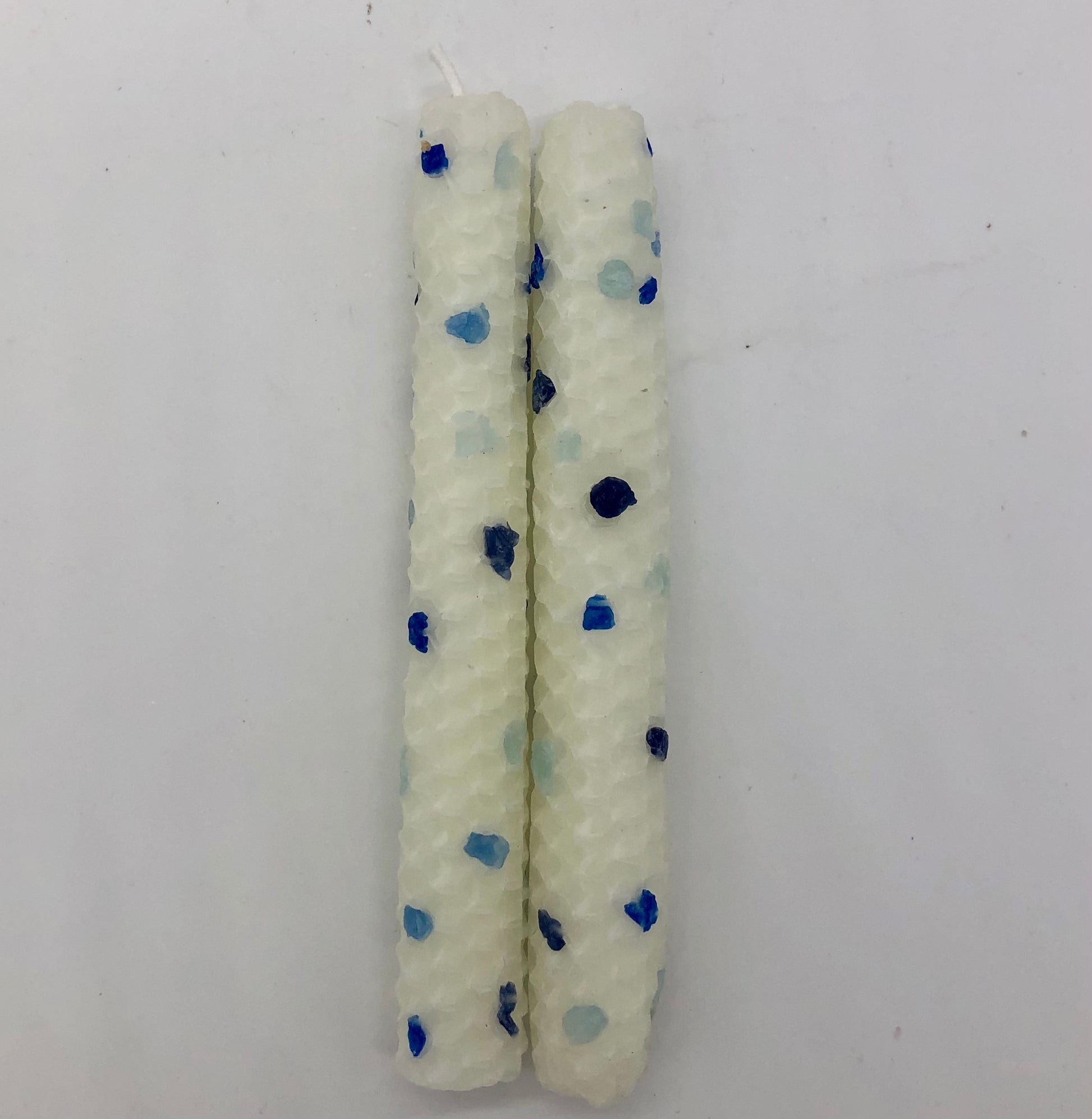 Two white shabbat candles with dots of color in four shades of blue.