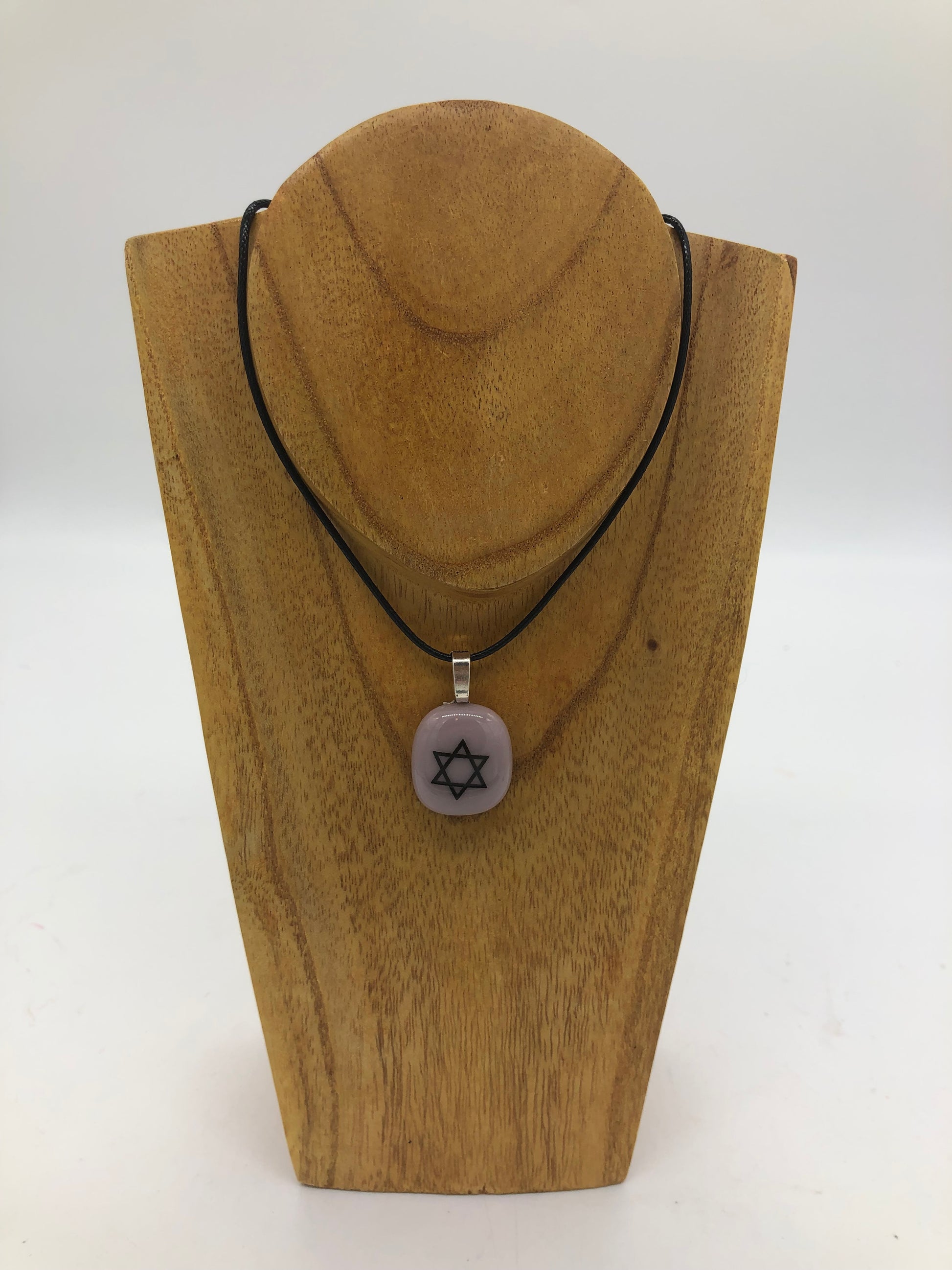Fused glass necklace on a black cord, displayed on wooden holder.  Necklace design is a mauve circle with white star of David. 