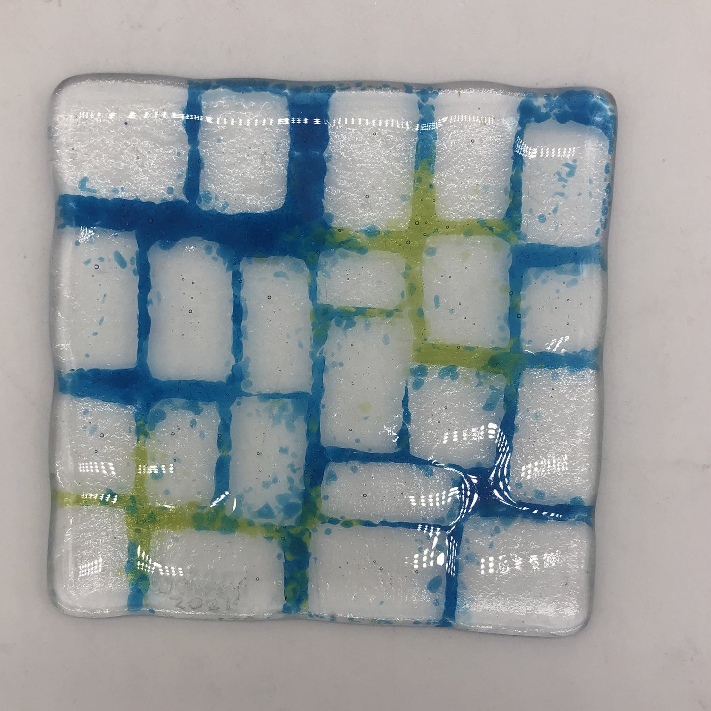 Clear square piece of glass with rectangles of clear and blue and green in the seams, mimicking grout.