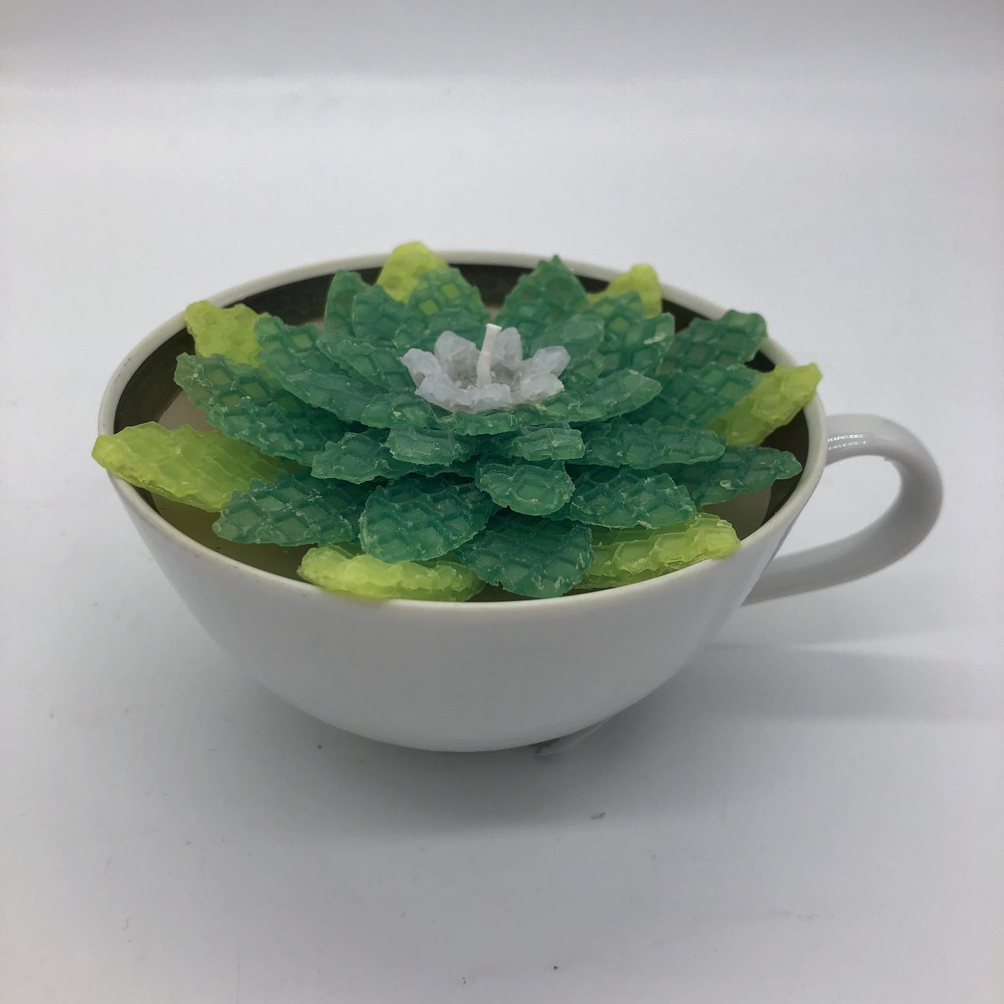 White tea cup filled with candle and shades of green beeswax succulent with lavender center on top