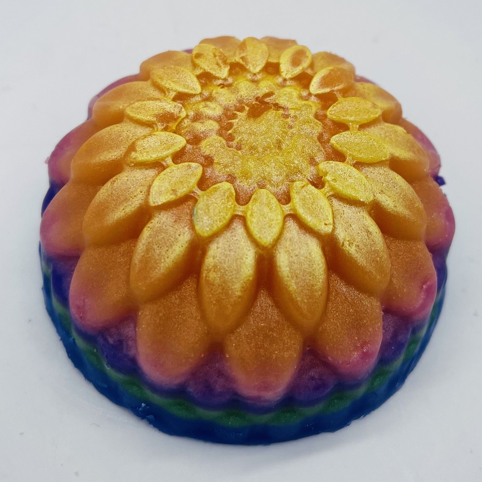 Round floral soap with layers in blue, green, purples, pink, orange and metallic yellow.