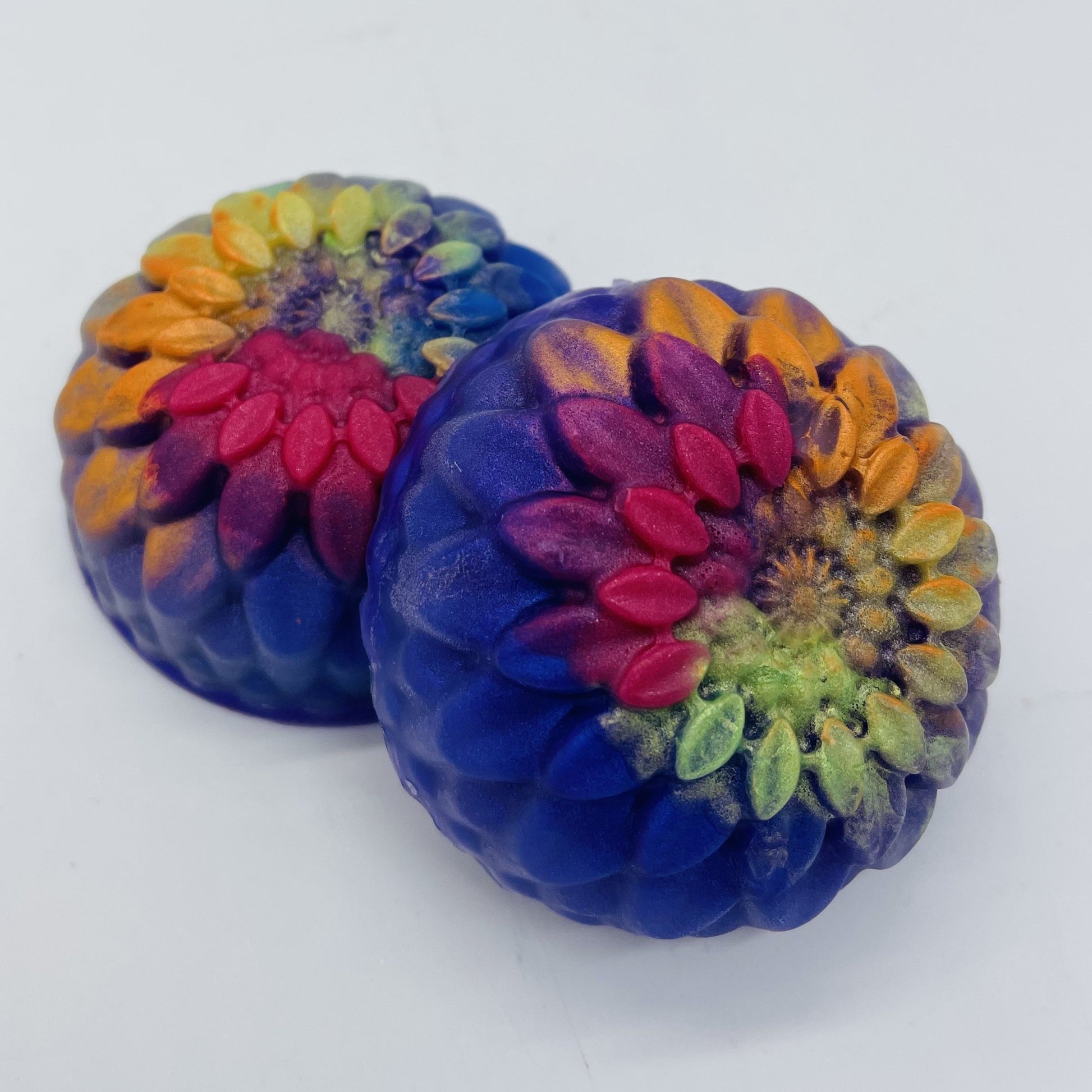 Two round floral soaps with deep blue bases and extra colors on top in pink, orange and yellow.