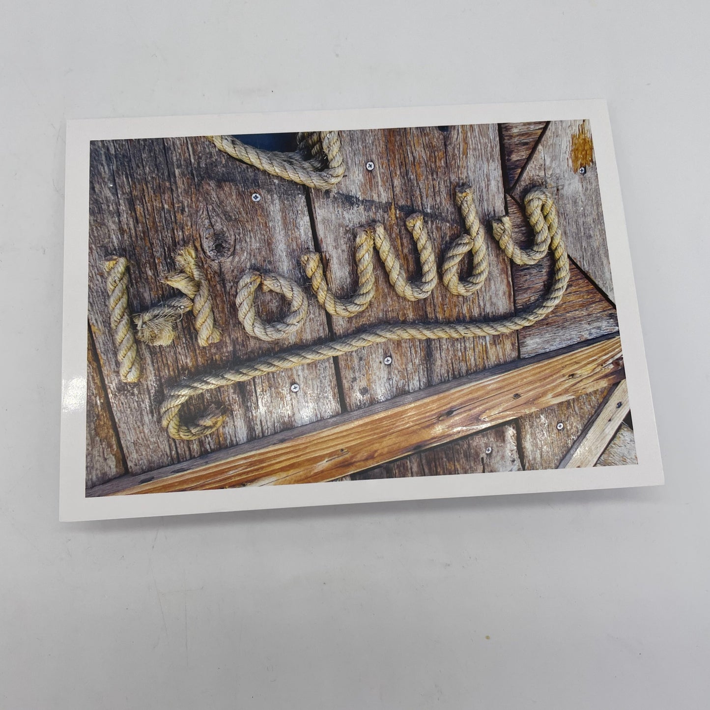 Rectangular greeting card with photograph of a wooden background and HOWDY written with rope.