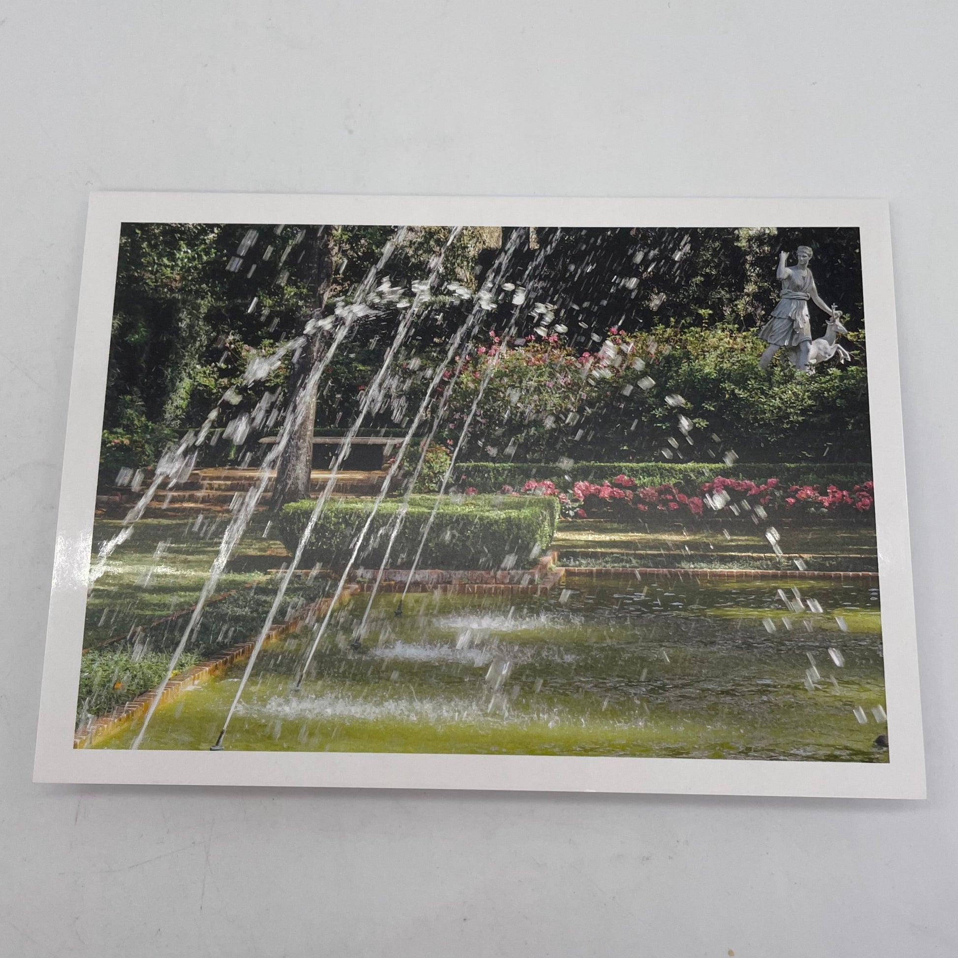 Greeting card with photograph of water and fountain with flowers and statue in the background.