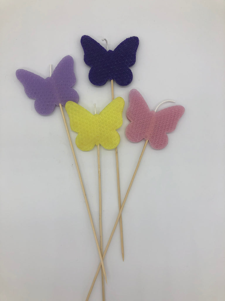 Four butterfly shaped candles at the end of a long wood skewer.  THe candles are lavender, purple, yellow and pink.