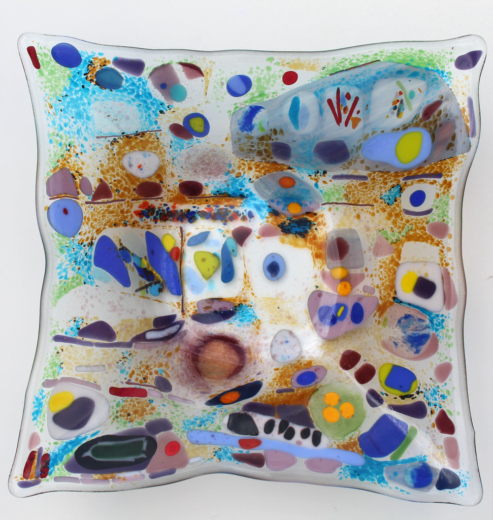 This is a piece of glass art with severl abstract shapes. The colors include blue, purple, red,orange, and green. It is a very unique design
