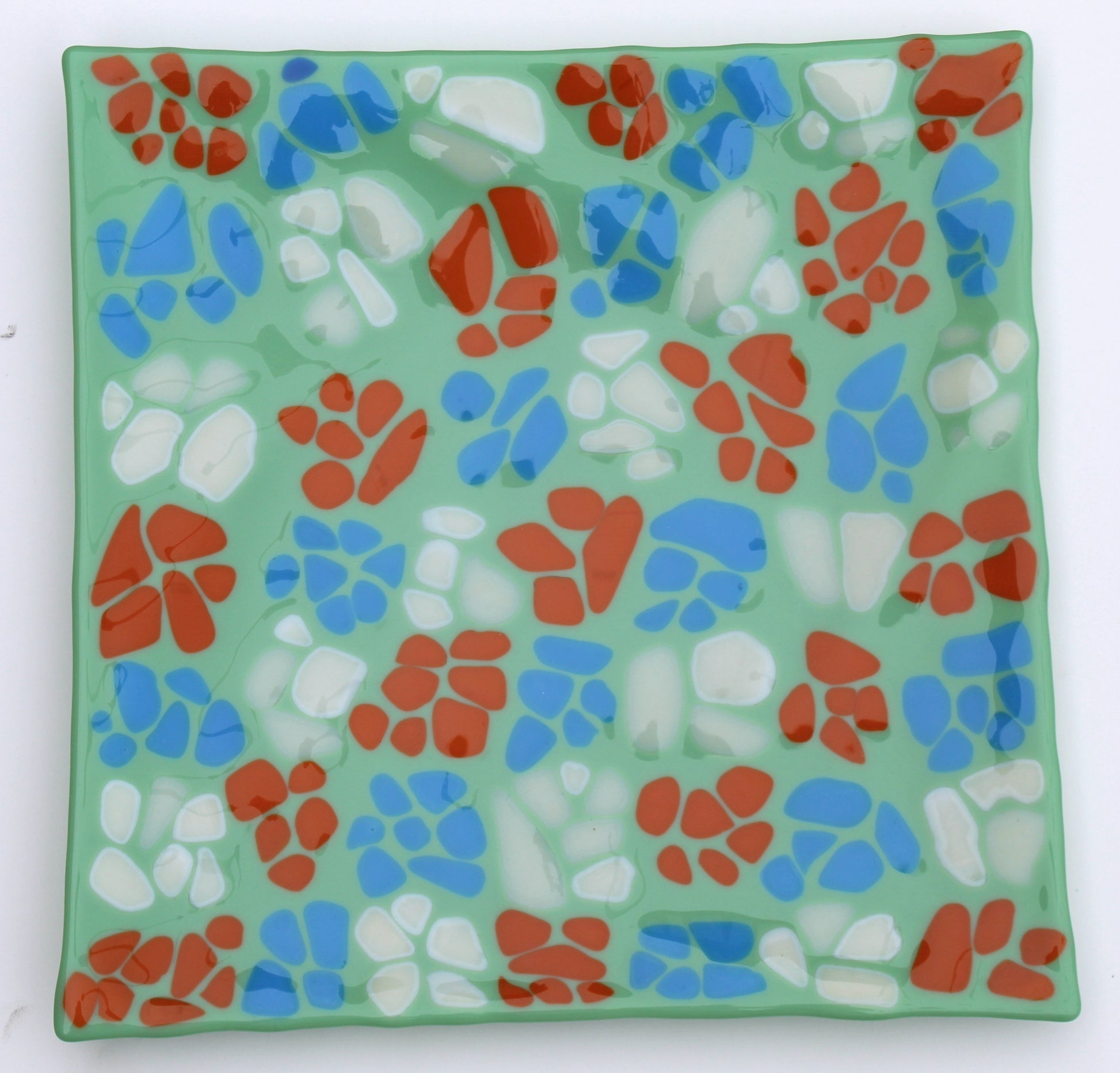 light green glass square plate with a diagonal pattern of repeating colors of white, orange, and blue