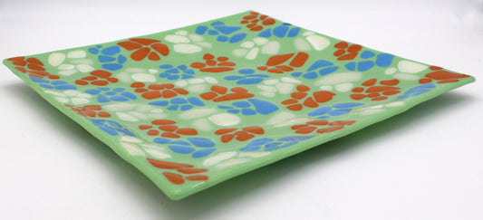 light green glass square plate with a diagonal pattern of repeating colors of white, orange, and blue
