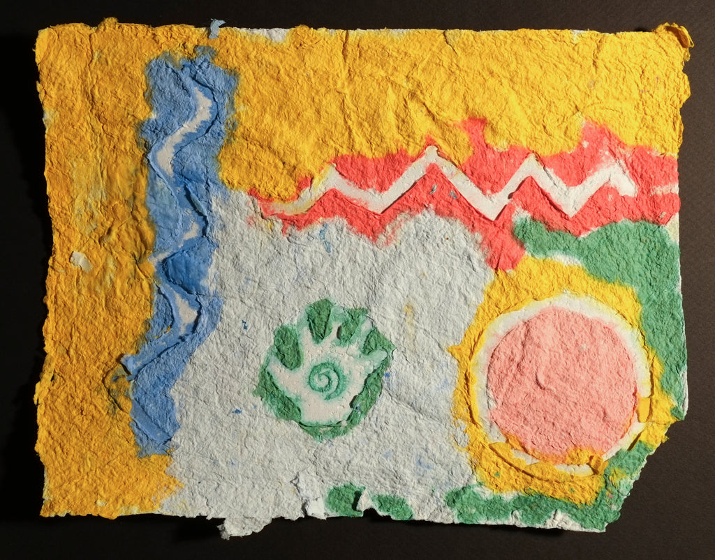 Highly textured handmade paper with the top edge and left being yellow, separated by blue and red zig zags. In the right corner is an embossed circle with green and yellow surrounding it with red inside. In the center (which is mostly the color of the paper) is a small hand with a spiral inside surrounded with an outline of green