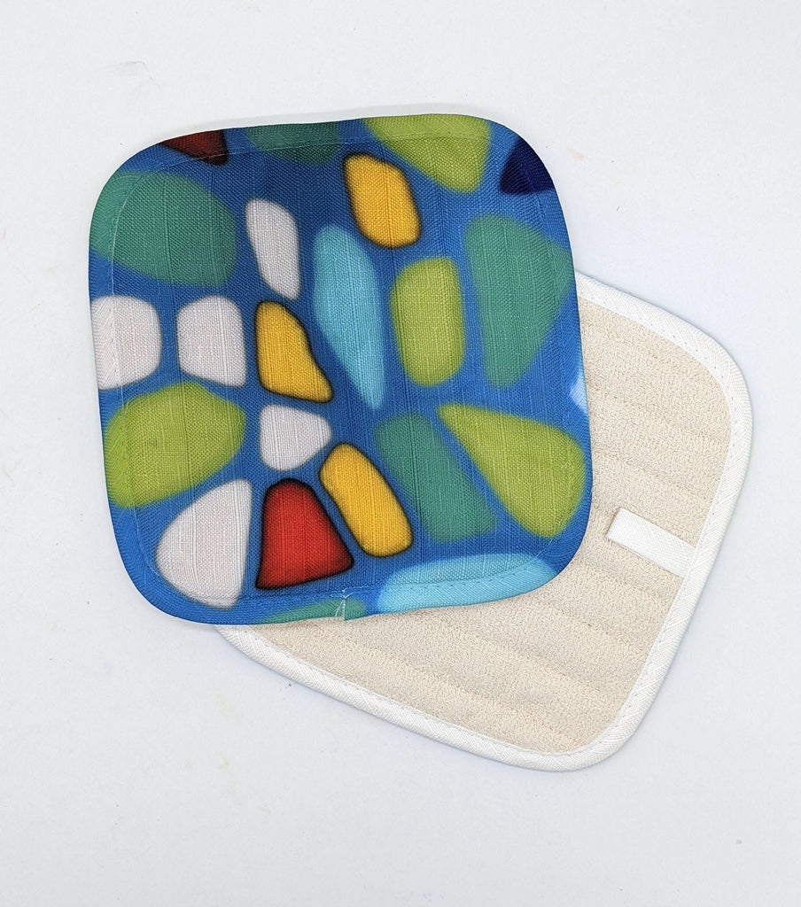 This is a potholder with a plain white back. On the front there is the following artwork: This is a sqaure fused glass piece with a blue background. There are pale blue, green, dark blue, red, yellow and white shapes over it