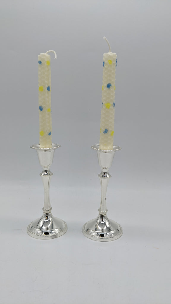 pair of white shabbat candles with yellow and blue confetti dots all over