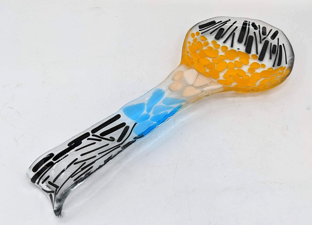 glass spoon rest in the shape of a spoon with black, blue, yellow, and white