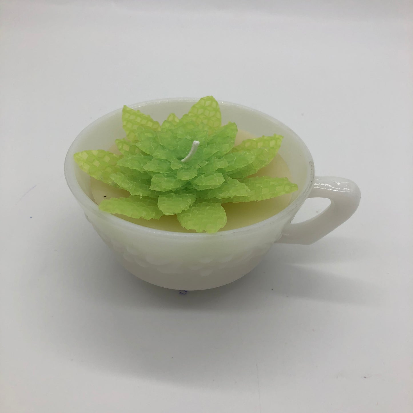 Milk glass teacup with light yellow candle and light green beeswax sheet succulent on top.