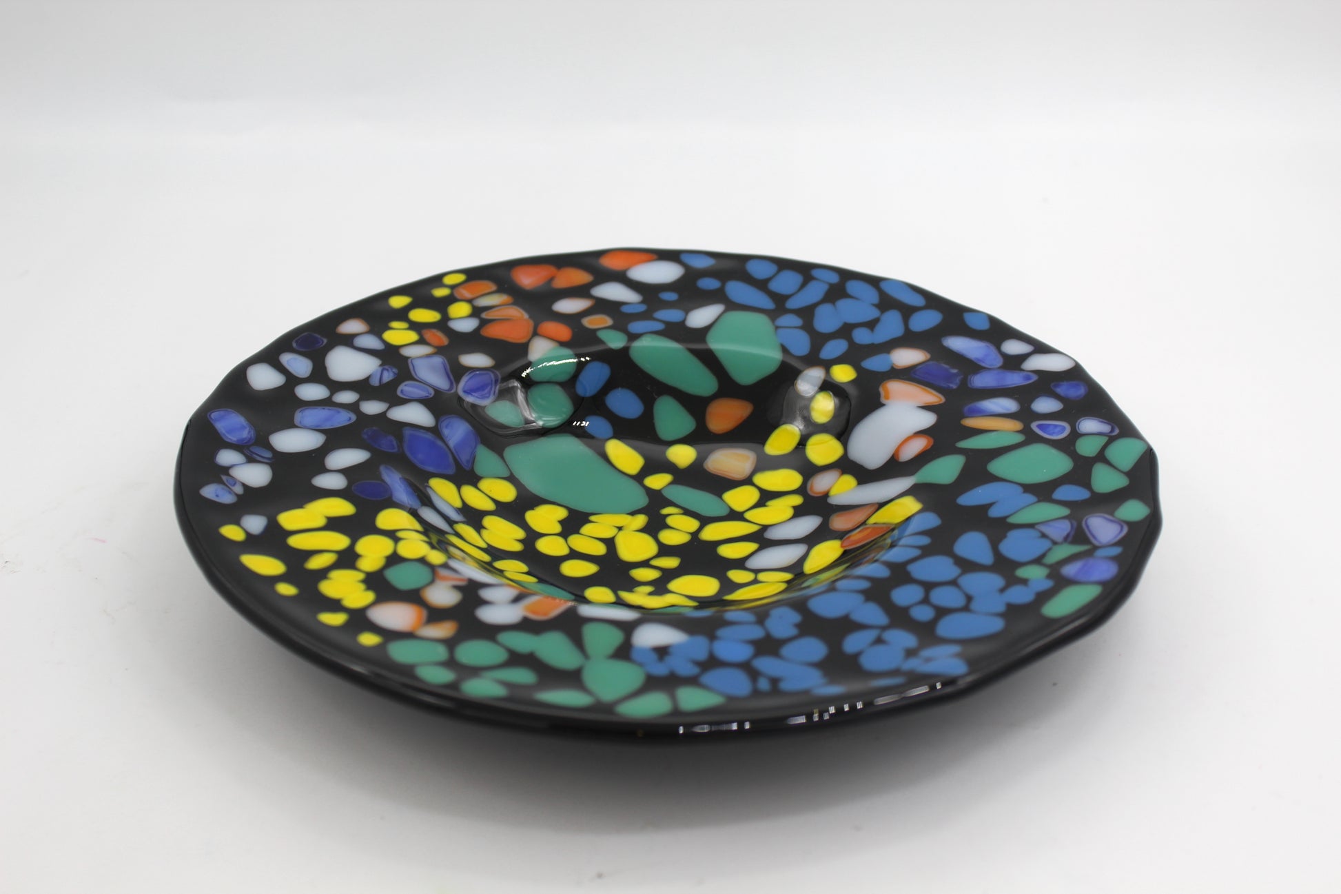 This is a black circular glass art with multicolored splotches including orange, blue, green, white and yellow.