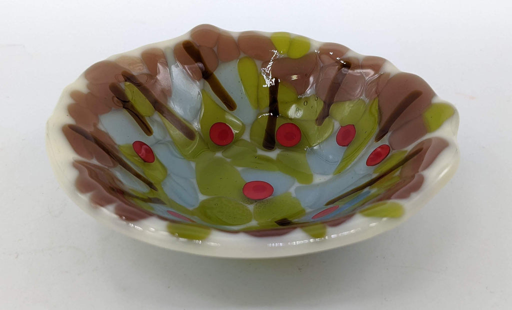 off white bowl filled with green, brown, and blue with a few red dots on top