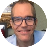 Man smiling, wearing blue framed glasses and has a buzz cut