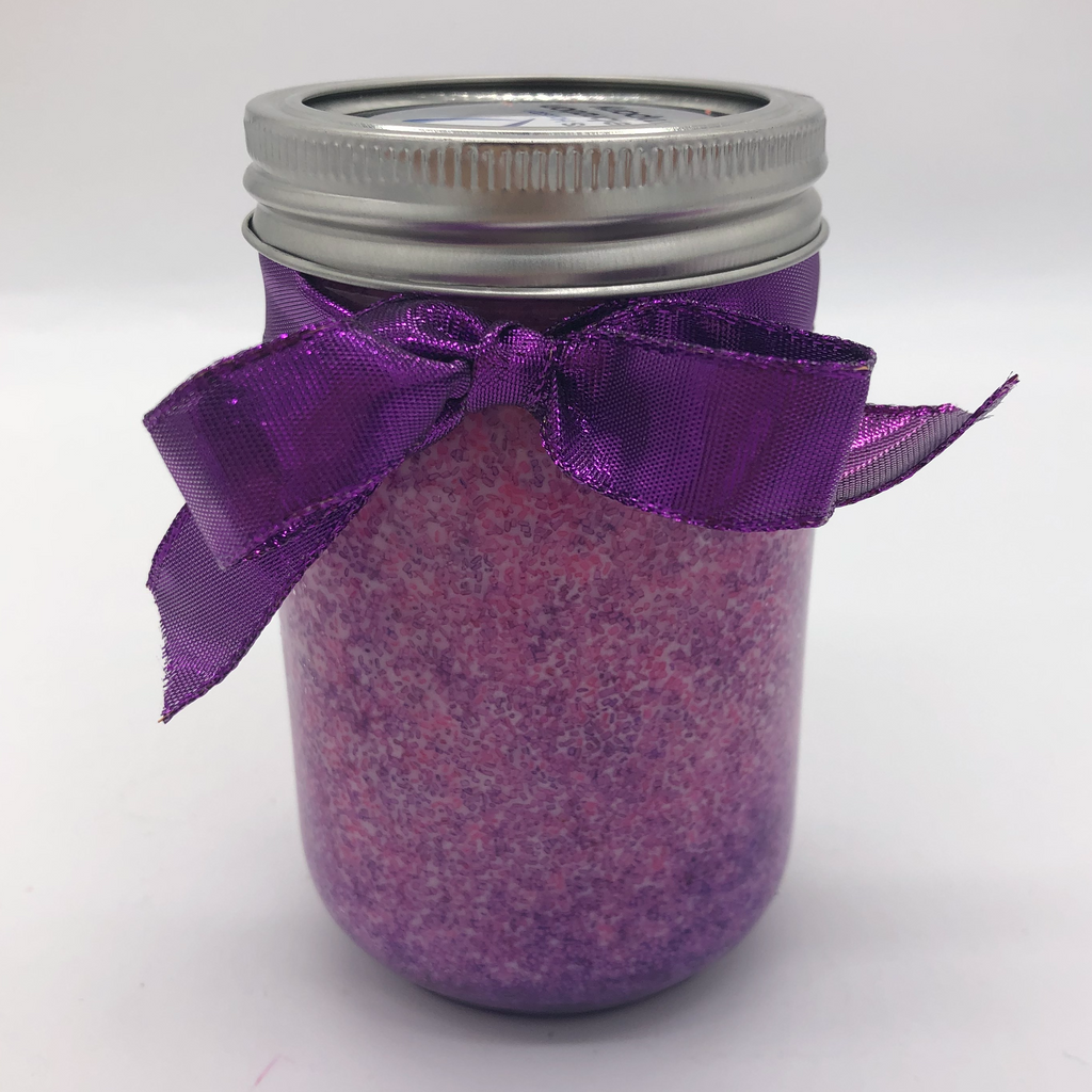 Canning jar with a white candle inside, pink and purple sugar crystals decorating the sides.  Purple metallic bow on the outside.