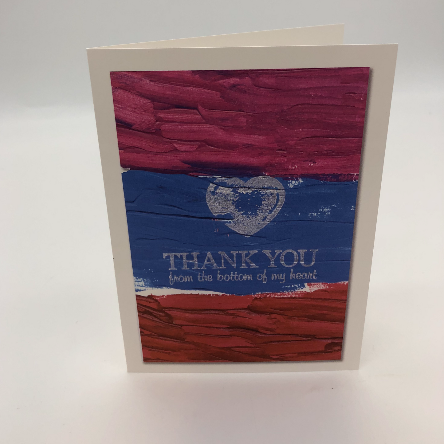 Print of an acrylic painting with stripes of three colors-maroon on top, bluish purple in the middle and red on bottom. Over the top is a white stamp of a heart and the words Thank you from the bottom of our heart.