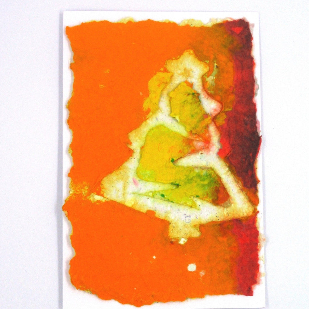 Handmade paper greeting card with orange and yellow background and white Christmas tree.