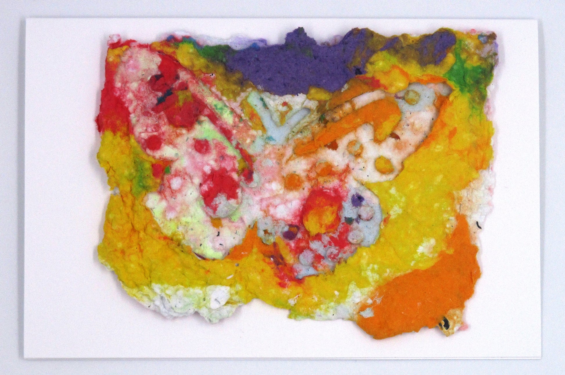 Handmade paper greeting card of purple, red, yellow and orange colors melted together in the background with a white butterfly over top