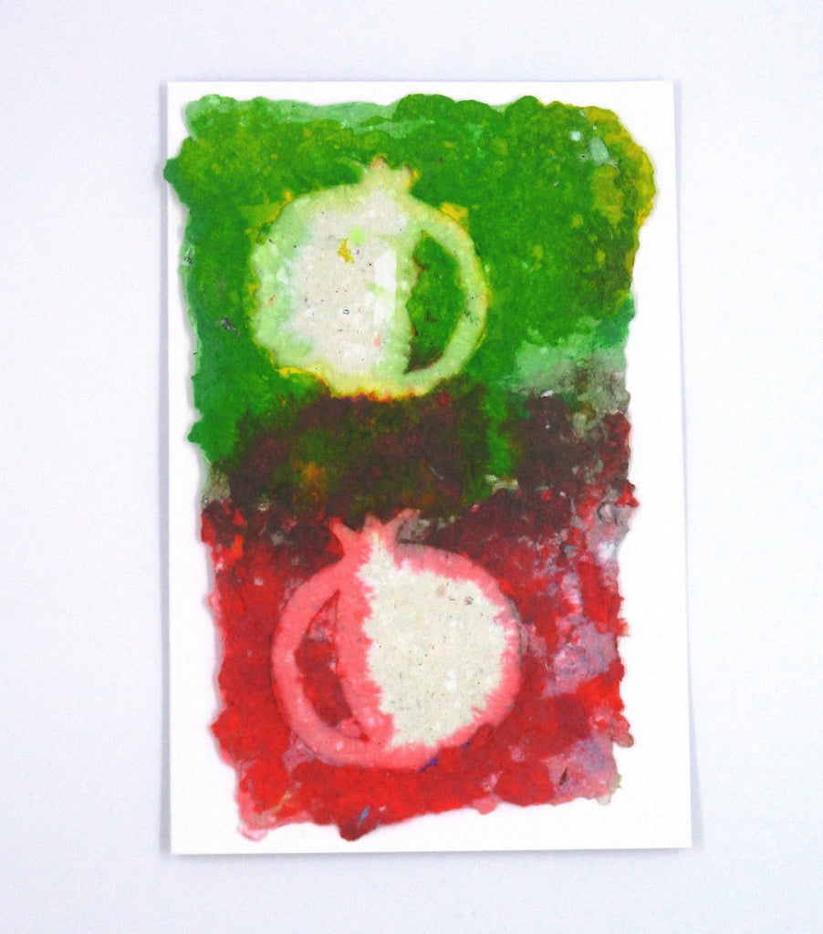 Handmade paper greeting card with two white pomegranates, the background is green on top, red on the bottom and the center a mixture of the two.
