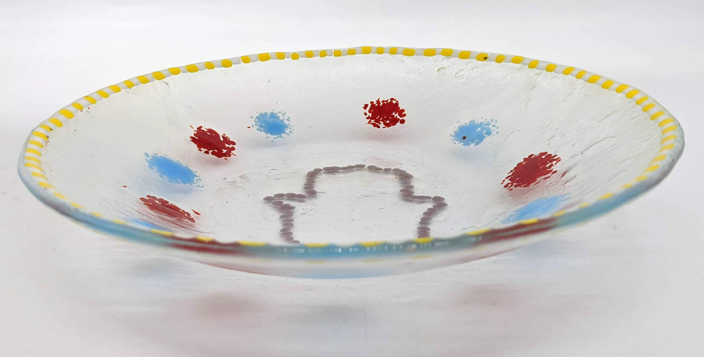 clear glass bowl with an outline of a hamsa in the center surrounded by alternating dots of blue and red with a border of yellow and white