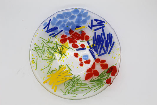 This is a clear circular glass art with blue, green and yellow lines. It has several red and blue abstract shapes as well
