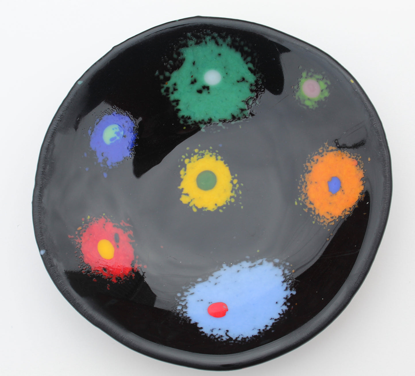 This is a black fused glass piece with green, orange, red, yellow and blue spattered dots with a multicolored dt in the center
