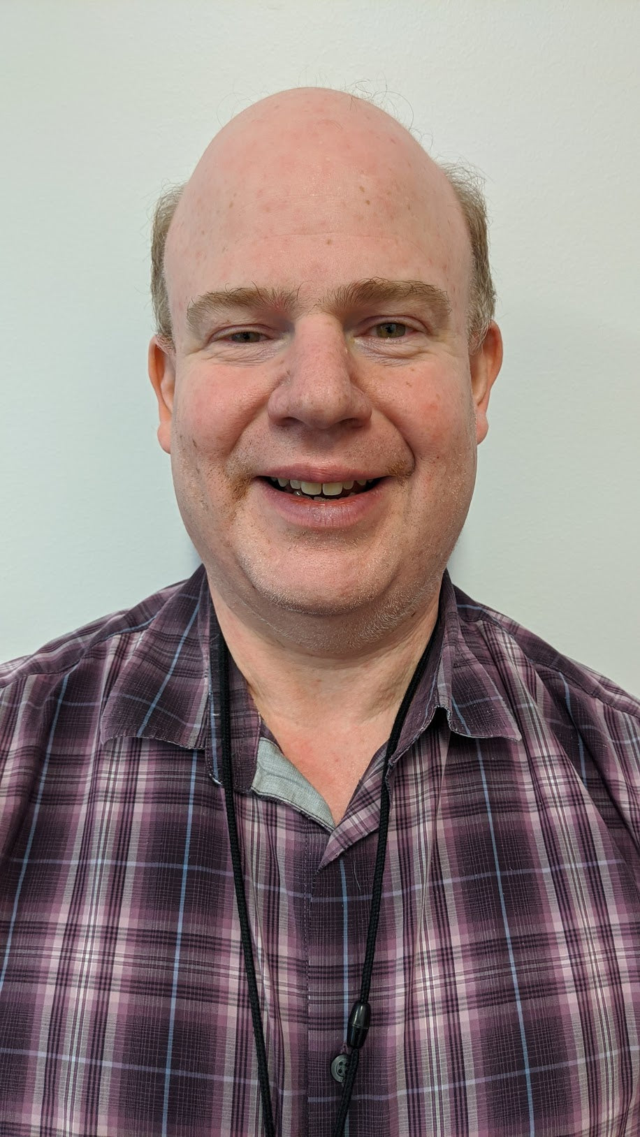 older man with receding hairline, smiling. Wearing a plaid colored shirt