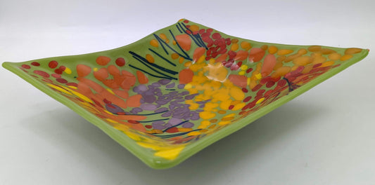 green glass square bowl covered in red, yellow, orange, and purple dots with navy lines