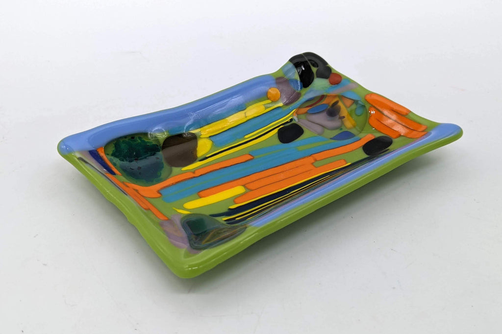 green glass soap dish with lines of blue, yellow, and orange interrupted by dots 