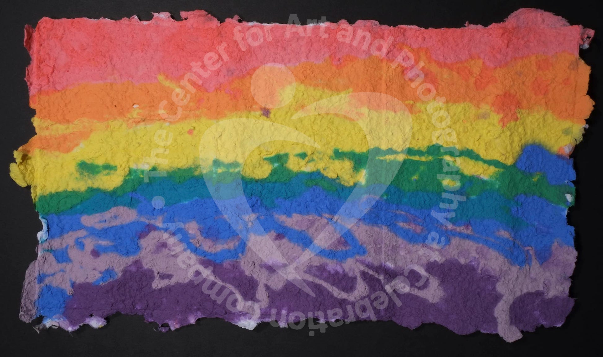 Highly textured handmade paper with horizontal lines of color (starting at the top) red, orange, yellow, green, blue, light purple, and dark purple.