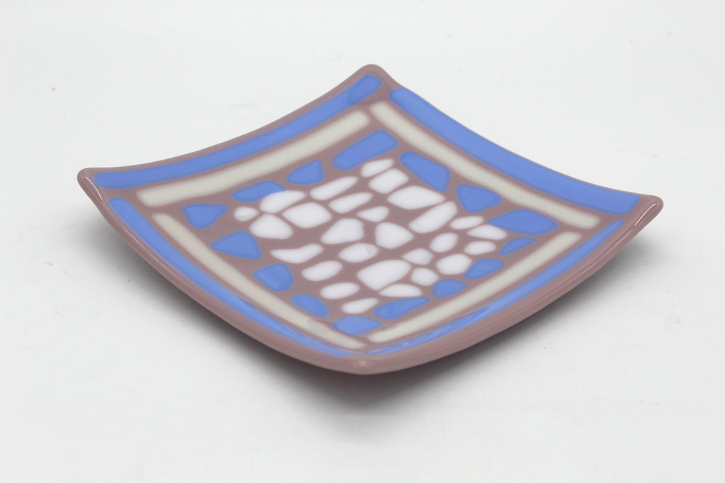 This is a glass sqaure piece of art that is purple It has blue and white lines outlining the edge of the piece, and blue and white splothces in the center