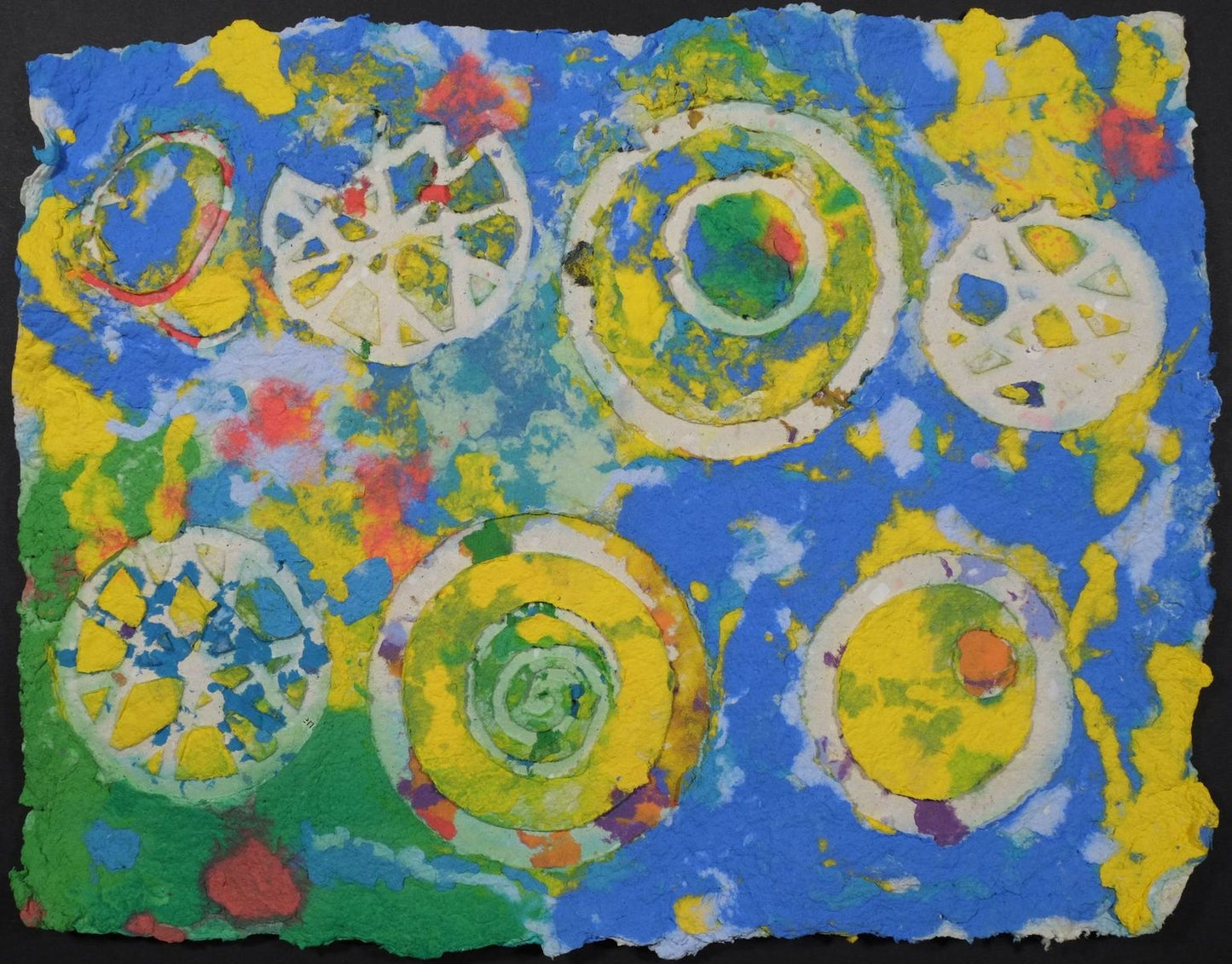Pigment on recycled paper artwork with white circles, swirls and wagon wheels against a background of blue, yellow, green and red