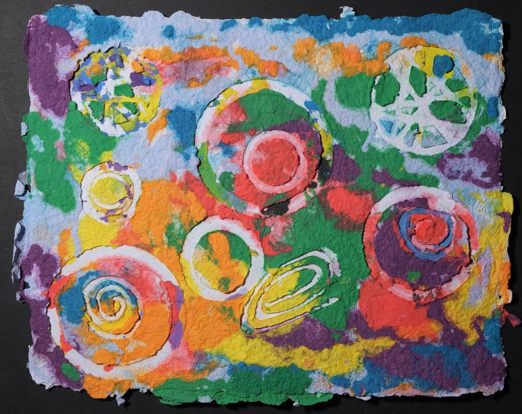 Pigment on recycled paper artwork with white circles, swirls and wagon wheels against a background of melted colors of blue, purple, green, red, orange and yellow