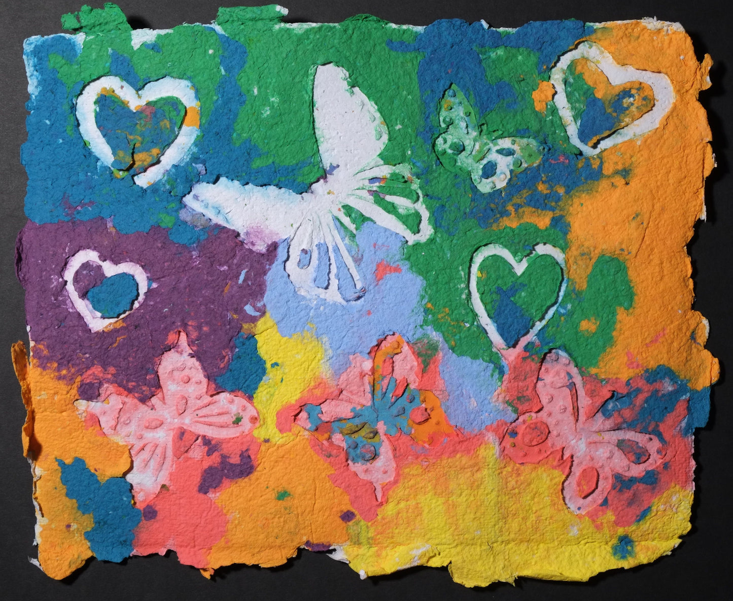 Highly textured handmade paper with white embossed butterflies and hearts against brightly colored oranges, greens, reds, and purple.